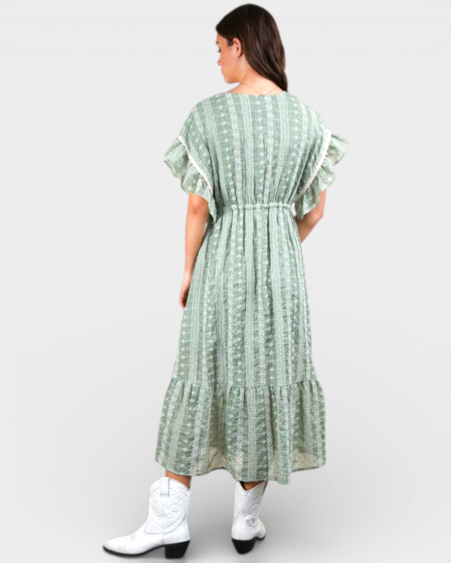 Woman wearing a green patterned dress with white boots on a white background