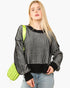 A blonde woman wearing a black and white vertically striped knit sweater with black ribbed trim, paired with light blue jeans and carrying a bright lime green quilted shoulder bag, set against a plain white background.
