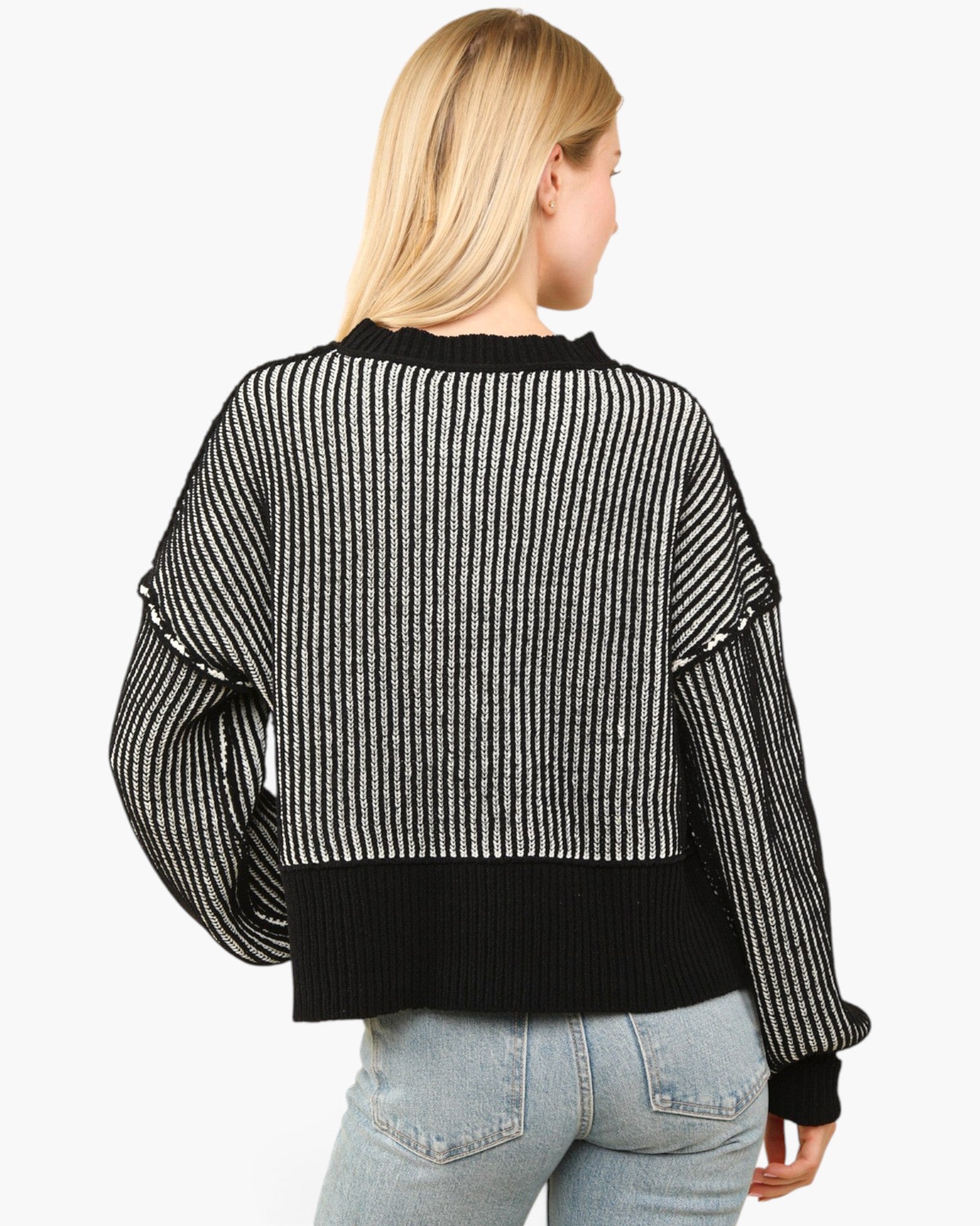 A woman shown from the back wearing a black and white vertically striped cropped sweater with solid black ribbed trim at the collar, hem, and cuffs, paired with light blue jeans against a plain white background.