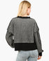 A woman shown from the back wearing a black and white vertically striped cropped sweater with solid black ribbed trim at the collar, hem, and cuffs, paired with light blue jeans against a plain white background.