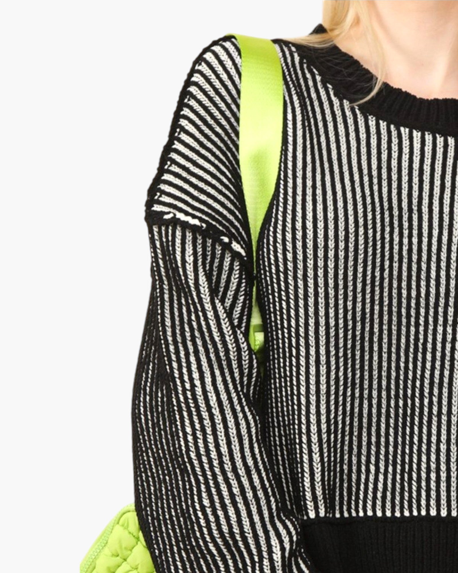 Close-up of a person wearing a black and white vertically striped knit sweater with a bright neon green shoulder strap and a matching neon green quilted bag visible against a light gray background.