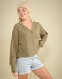 Woman wearing a green sweater and denim shorts against a beige background
