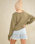 Person wearing a green sweater and light blue shorts with a beige beanie on a plain background