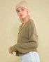 Woman wearing a beige knit beanie and olive green sweater against a beige background