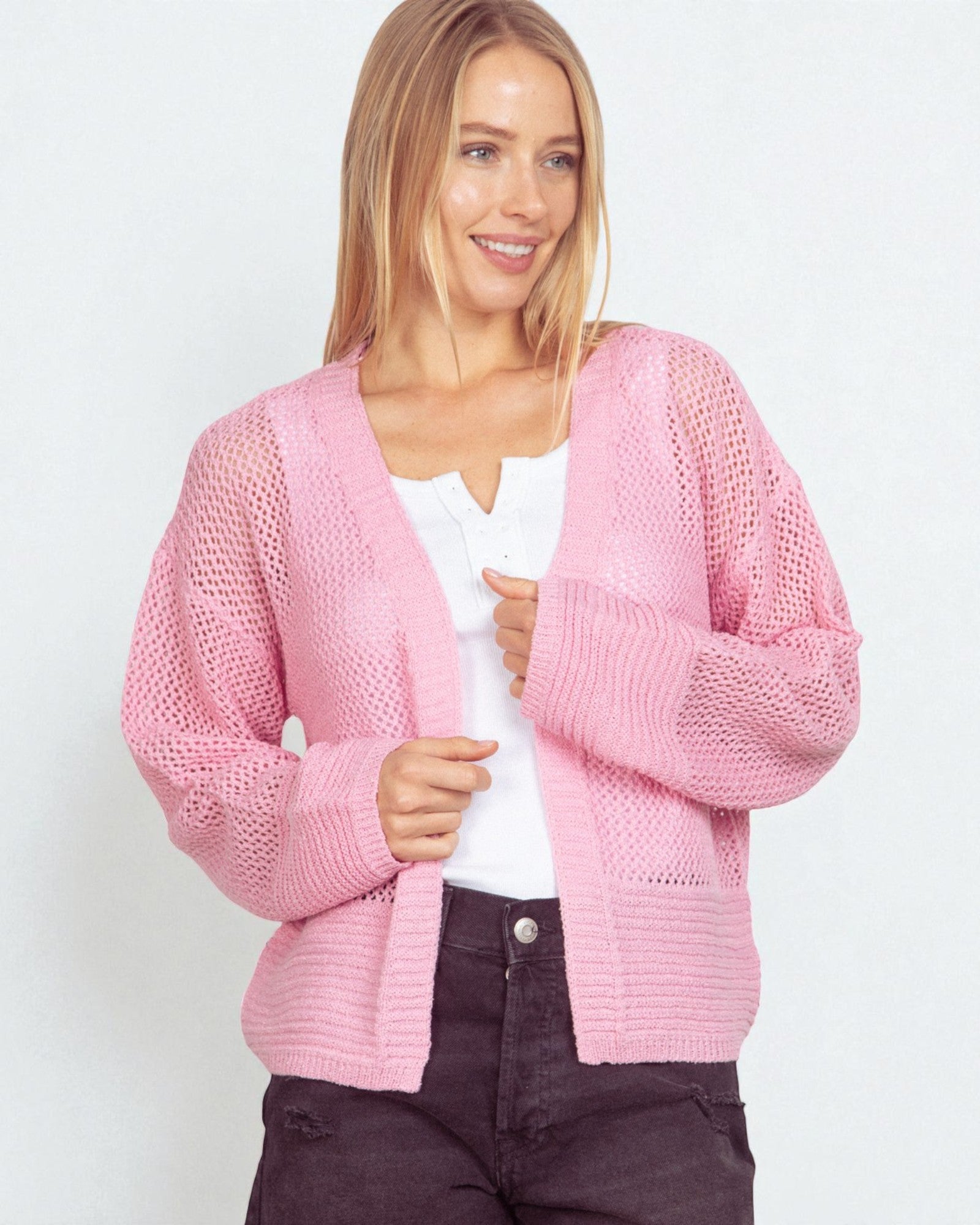 Woman wearing a pink knitted cardigan over a white shirt on a light background