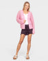 Woman wearing a pink cardigan over a white top and black shorts on a white background