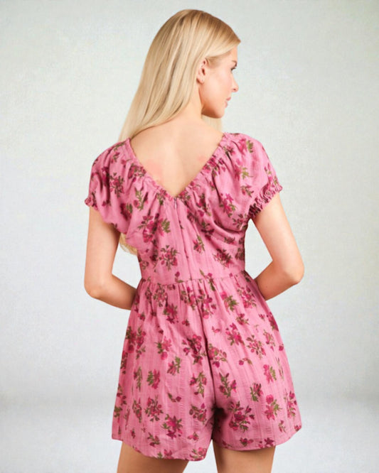 Woman wearing a pink floral romper on a plain background