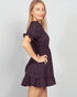 Woman wearing a dark purple dress with ruffled sleeves and hem on a light gray background
