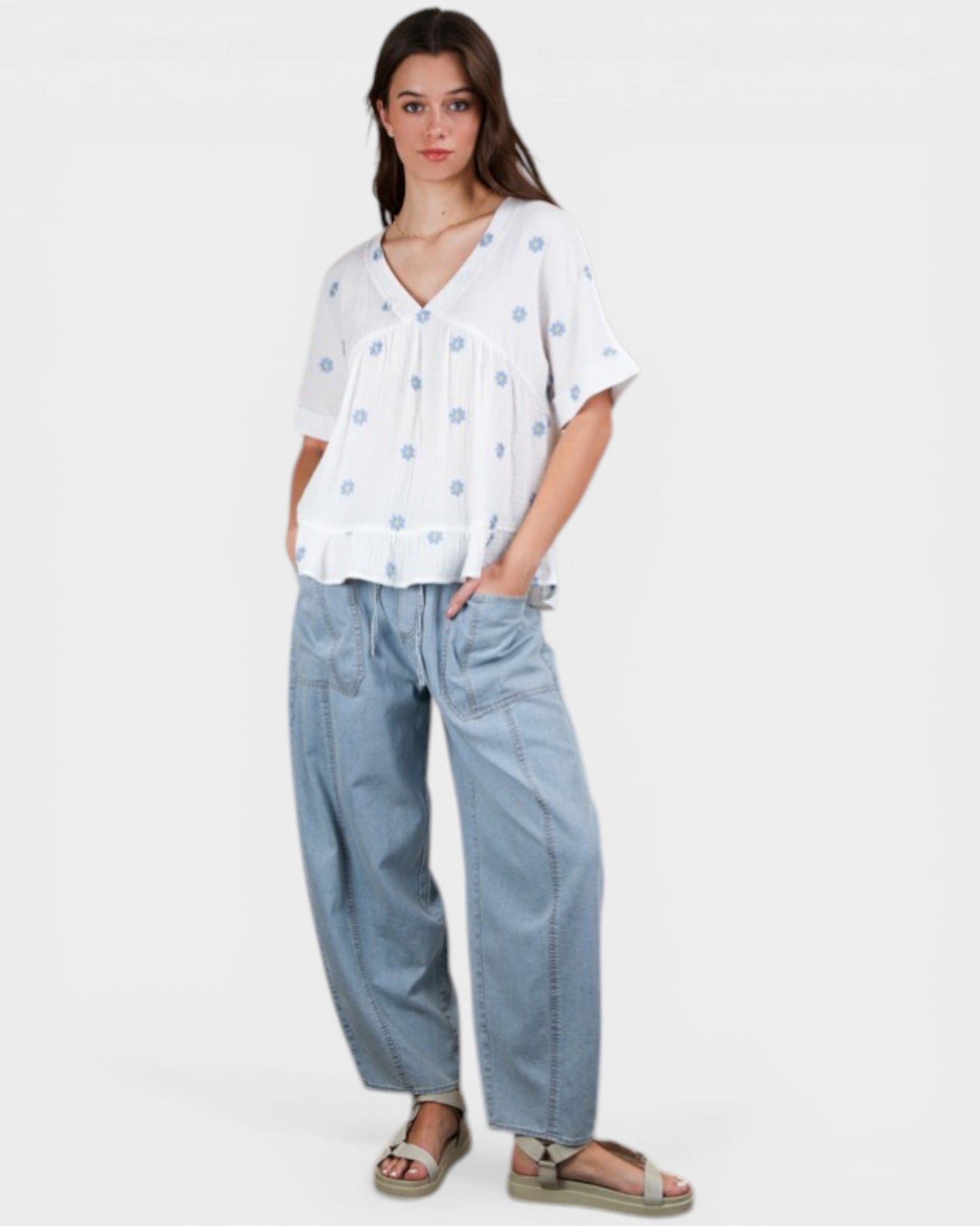 Woman wearing a white blouse with blue patterns and light blue jeans on a white background