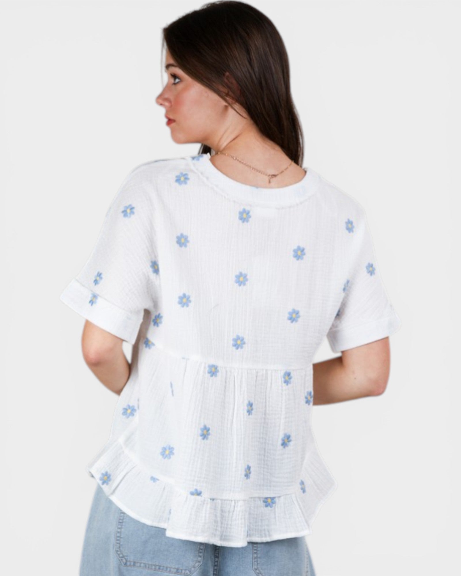 Woman wearing a white blouse with blue floral patterns on a plain background