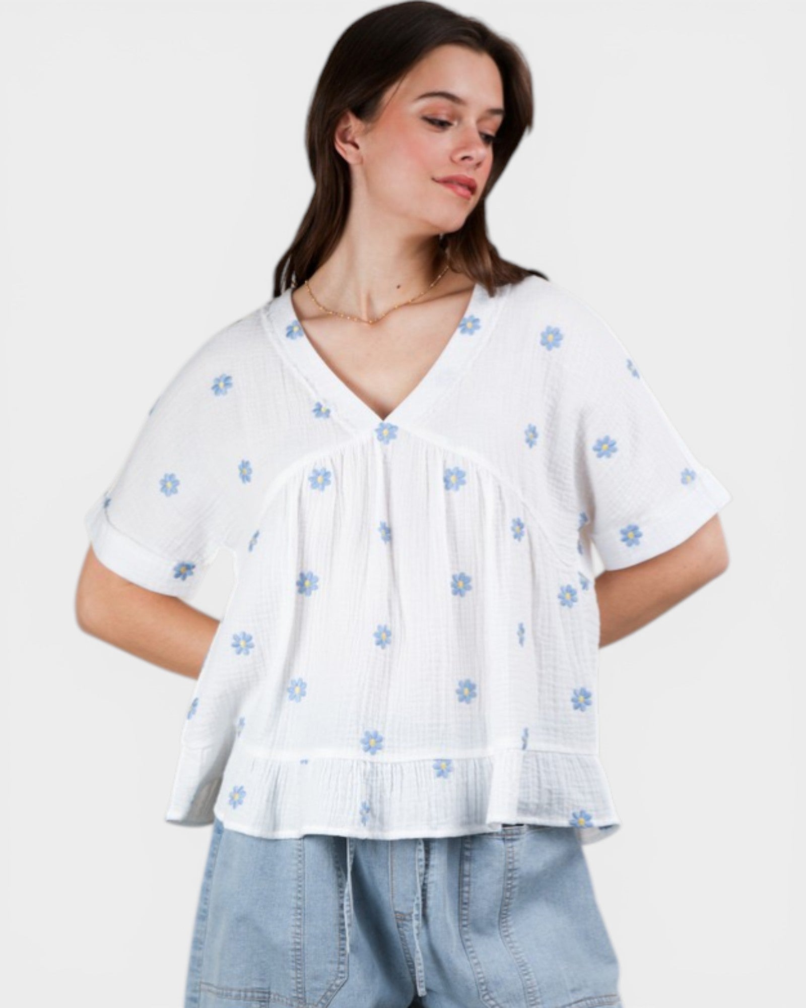 Woman wearing a white blouse with blue floral patterns and light blue jeans on a plain background