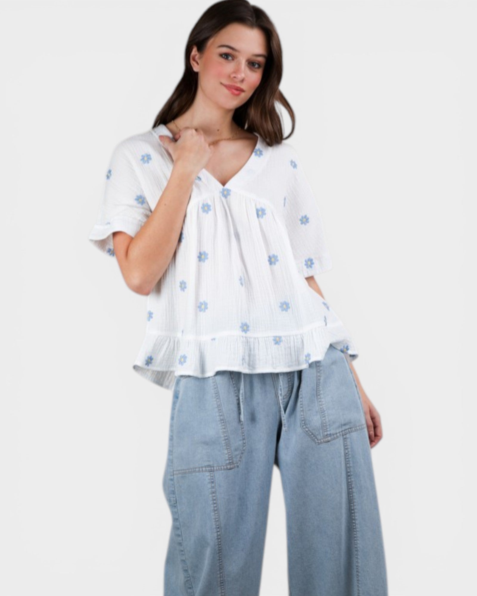 Woman wearing a white blouse with blue floral patterns and light blue jeans on a white background