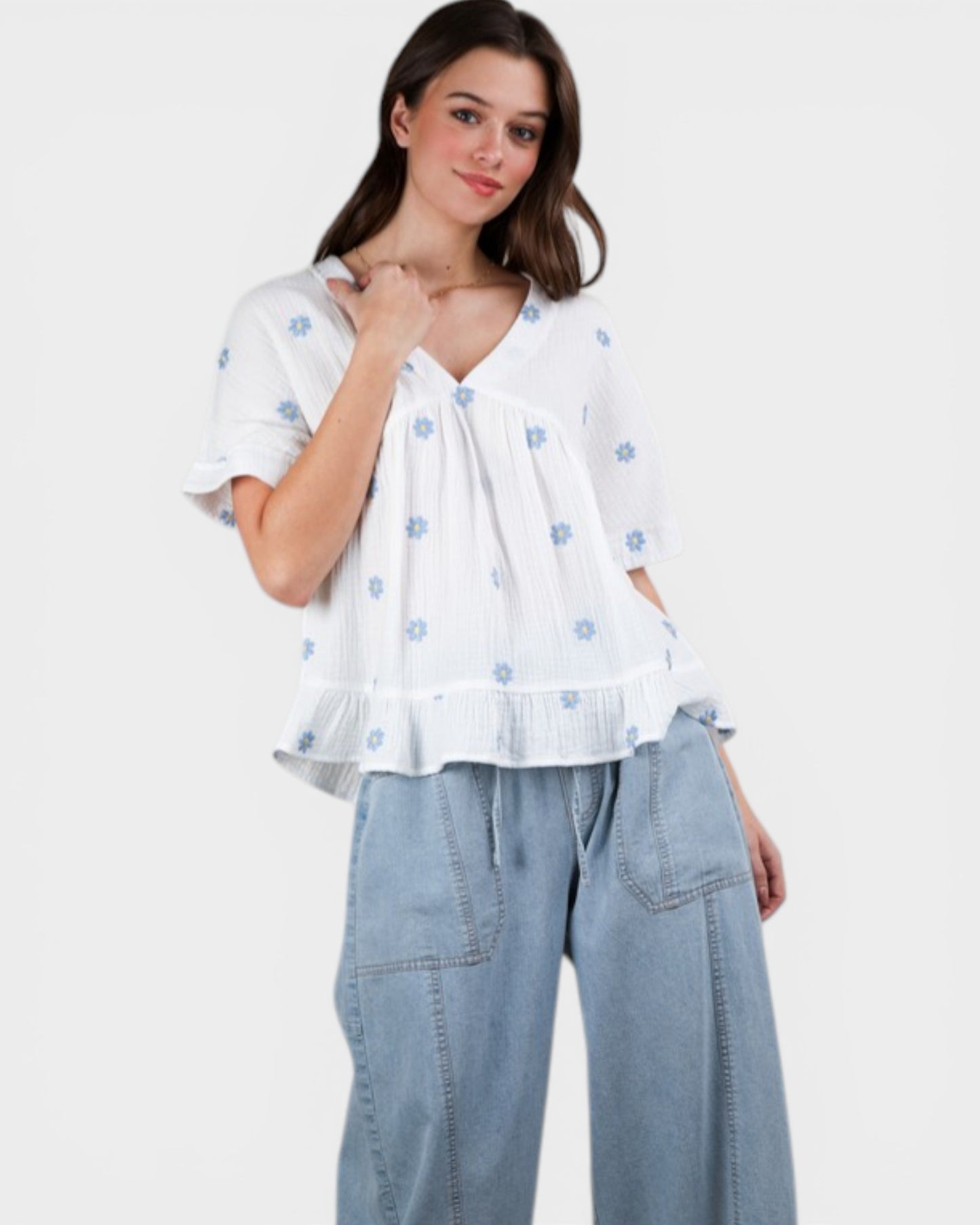 Woman wearing a white blouse with blue floral patterns and light blue jeans on a white background