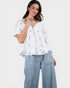 Woman wearing a white blouse with blue floral patterns and light blue jeans on a white background