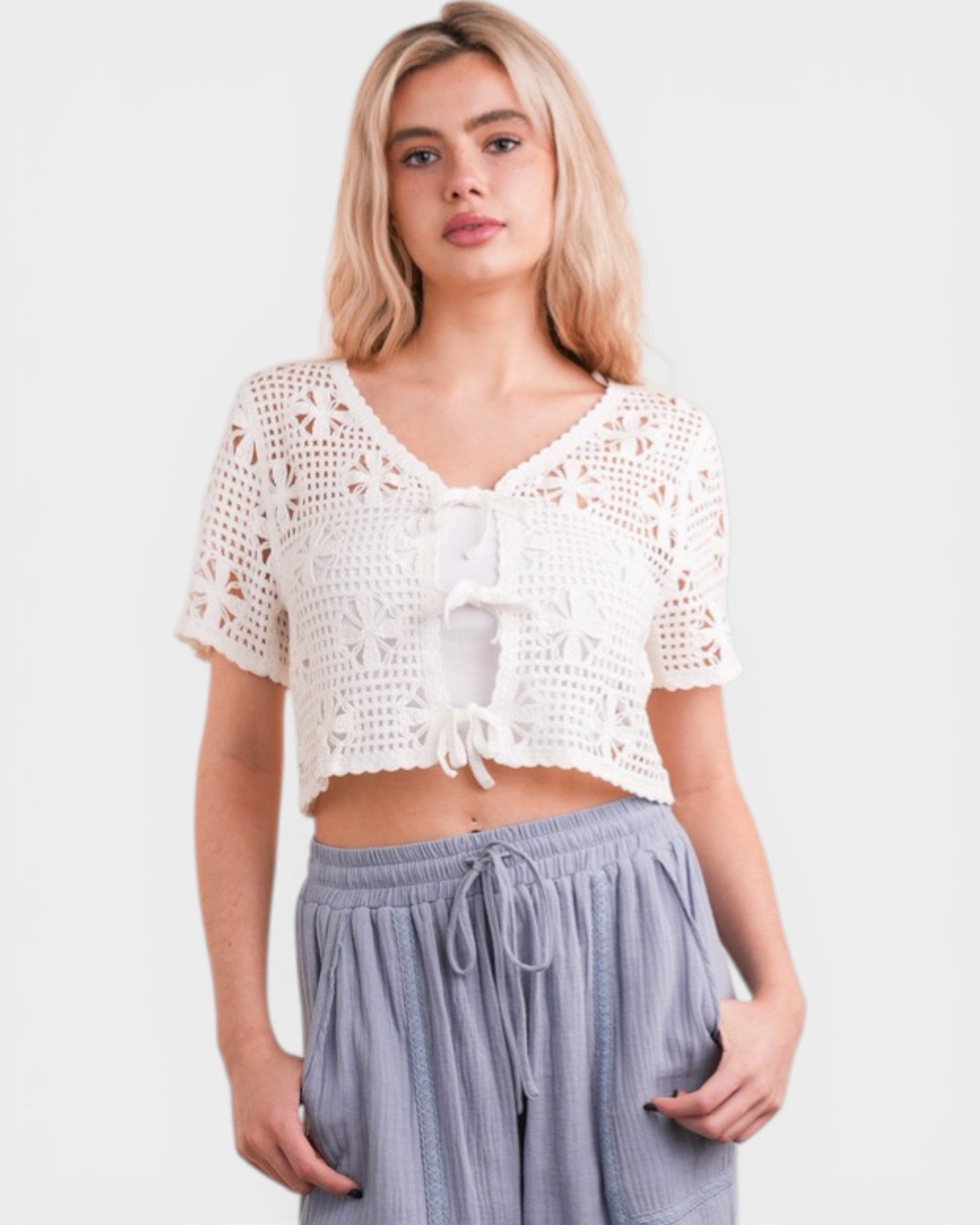 Woman wearing a white crochet top and light blue pants on a plain background