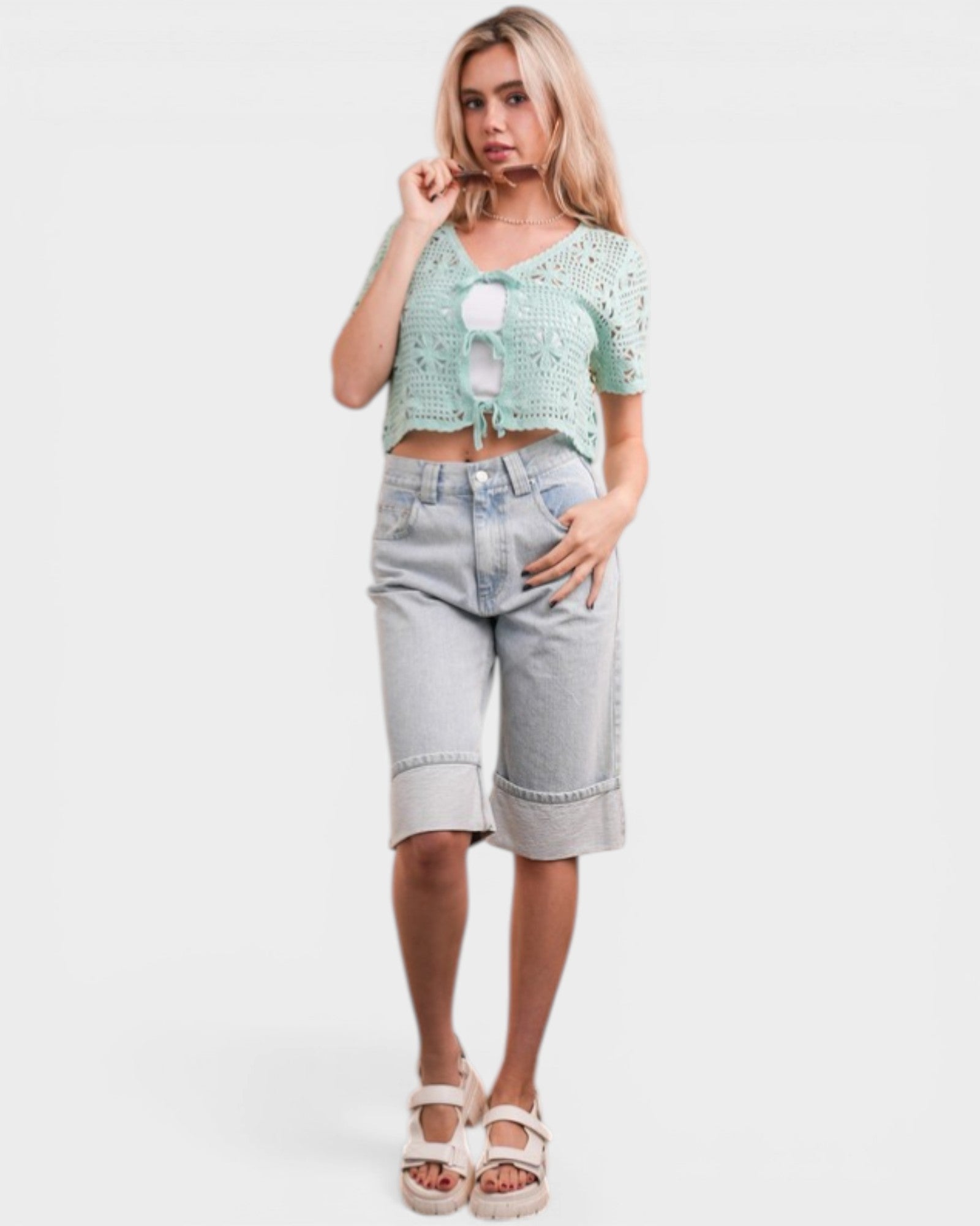Woman wearing a light green crop top and denim shorts on a white background