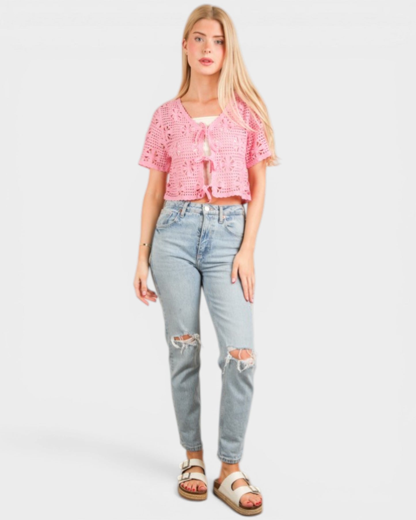 Woman wearing a pink lace top and light blue jeans on a white background