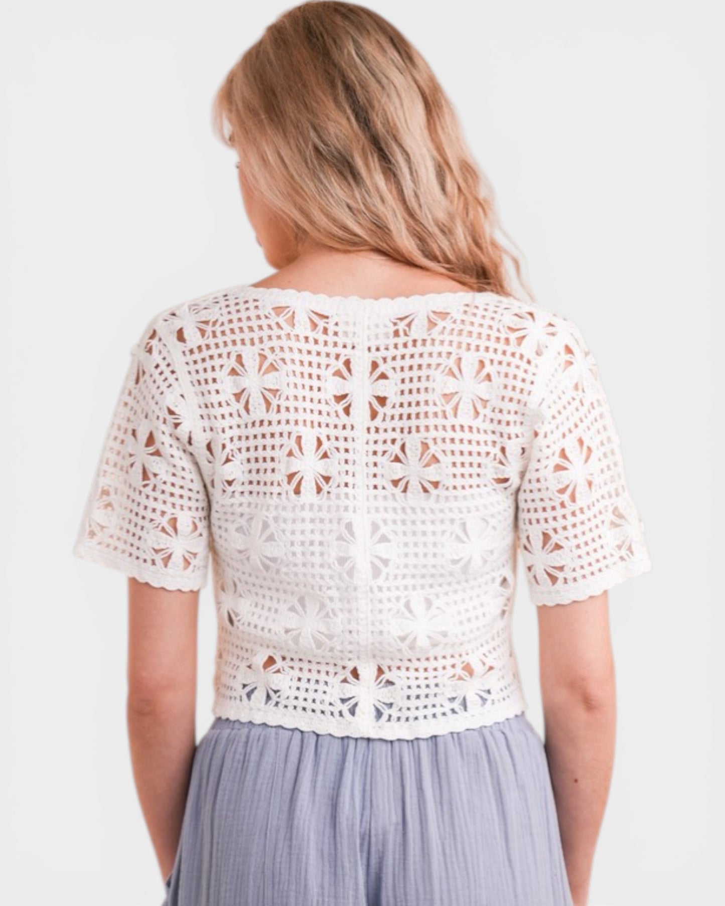 Woman wearing a white crochet top and gray skirt on a plain background