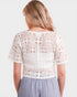 Woman wearing a white crochet top and gray skirt on a plain background