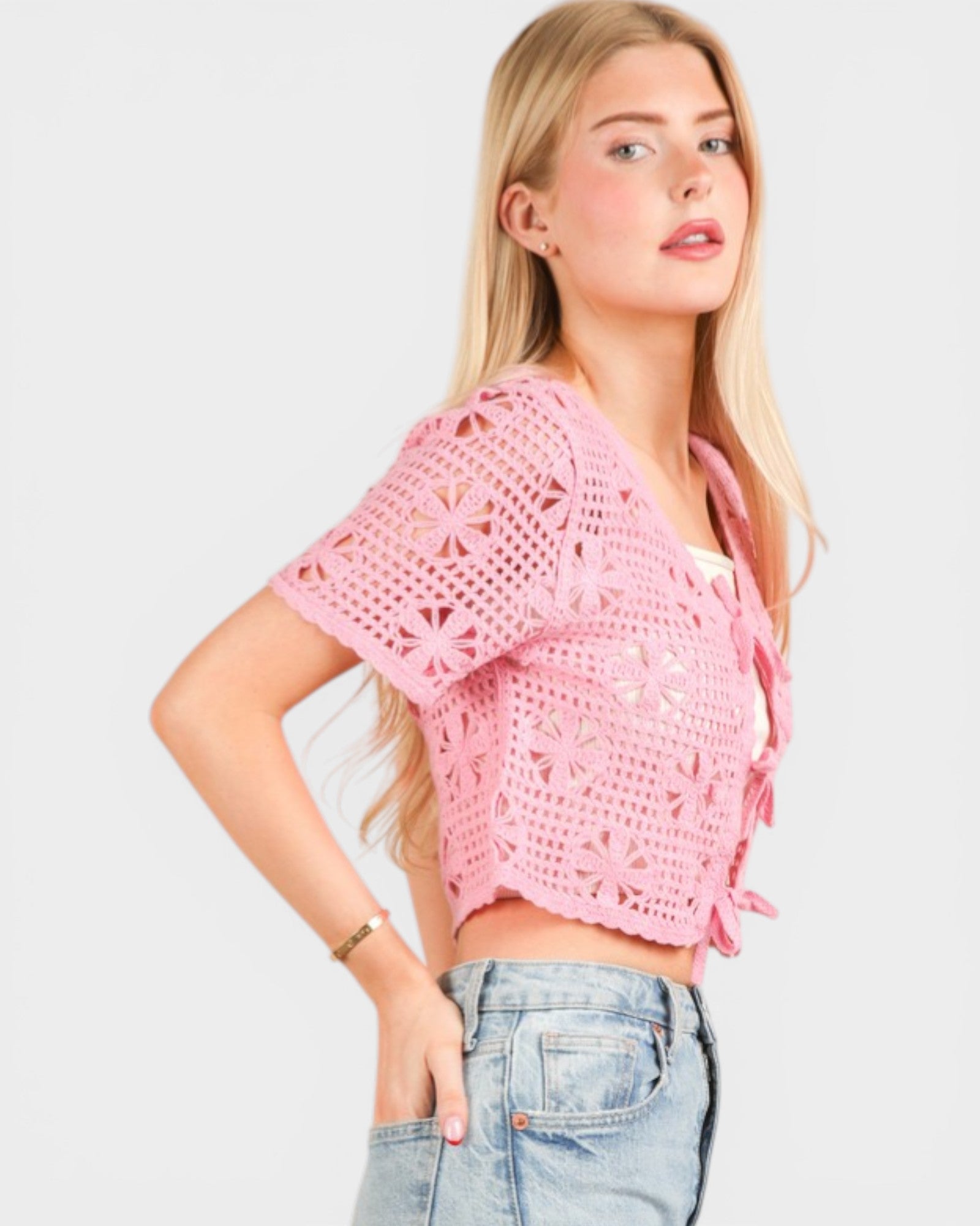 Woman wearing a pink crochet top and blue jeans on a light gray background