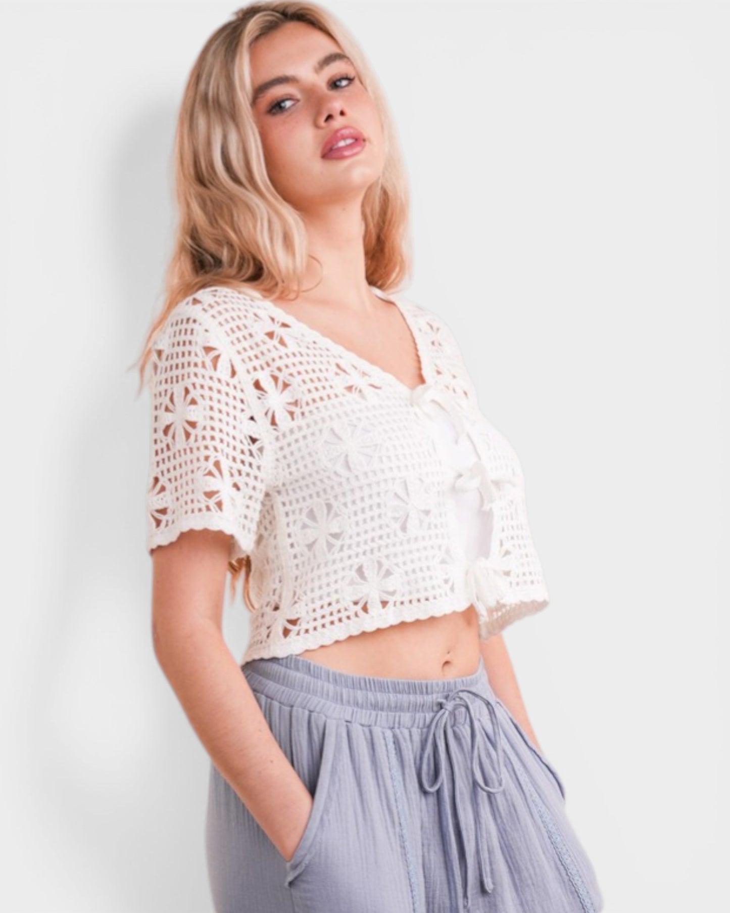Woman wearing a white crochet top and gray pants against a light background