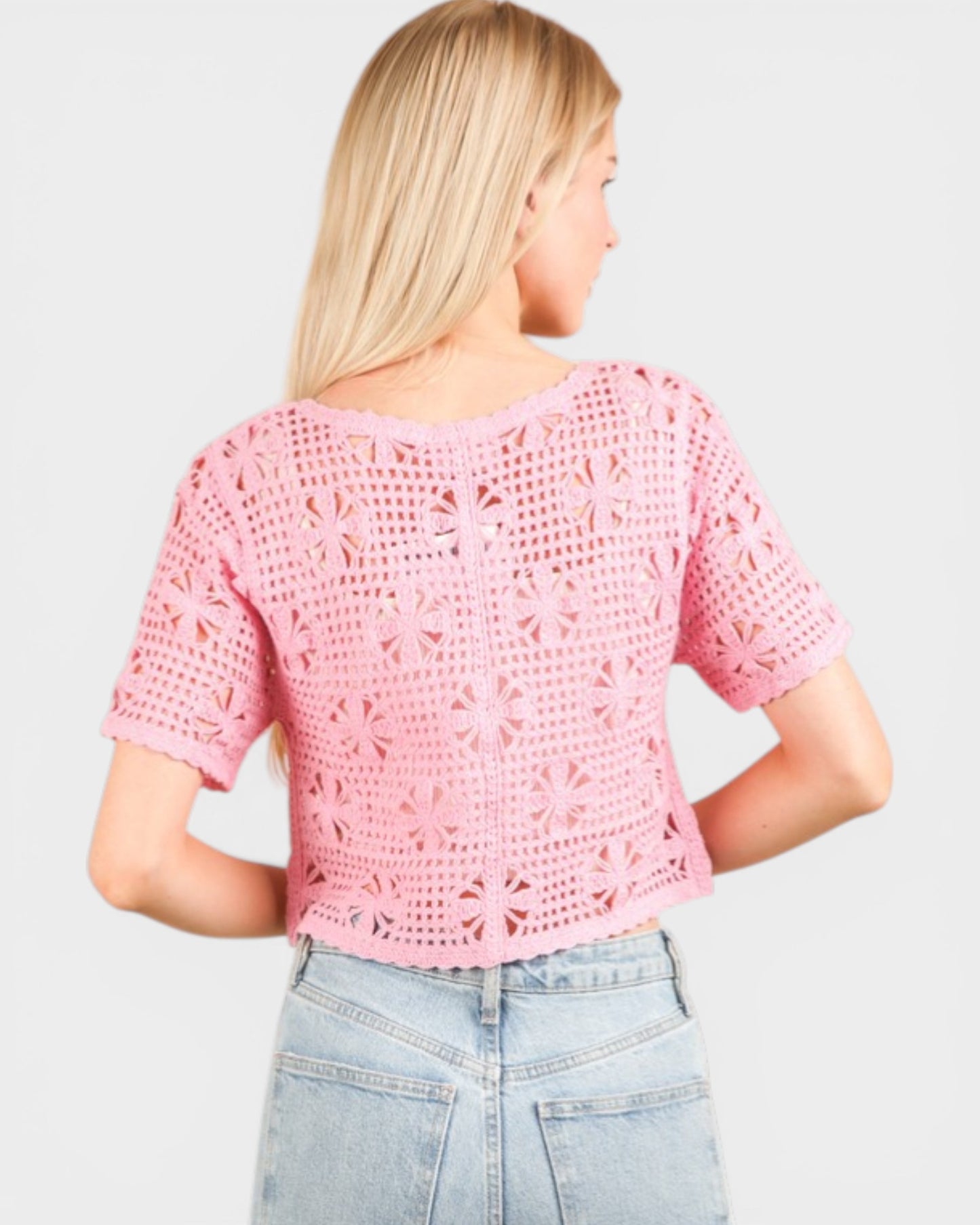 Person wearing a pink crochet top and light blue jeans on a plain background