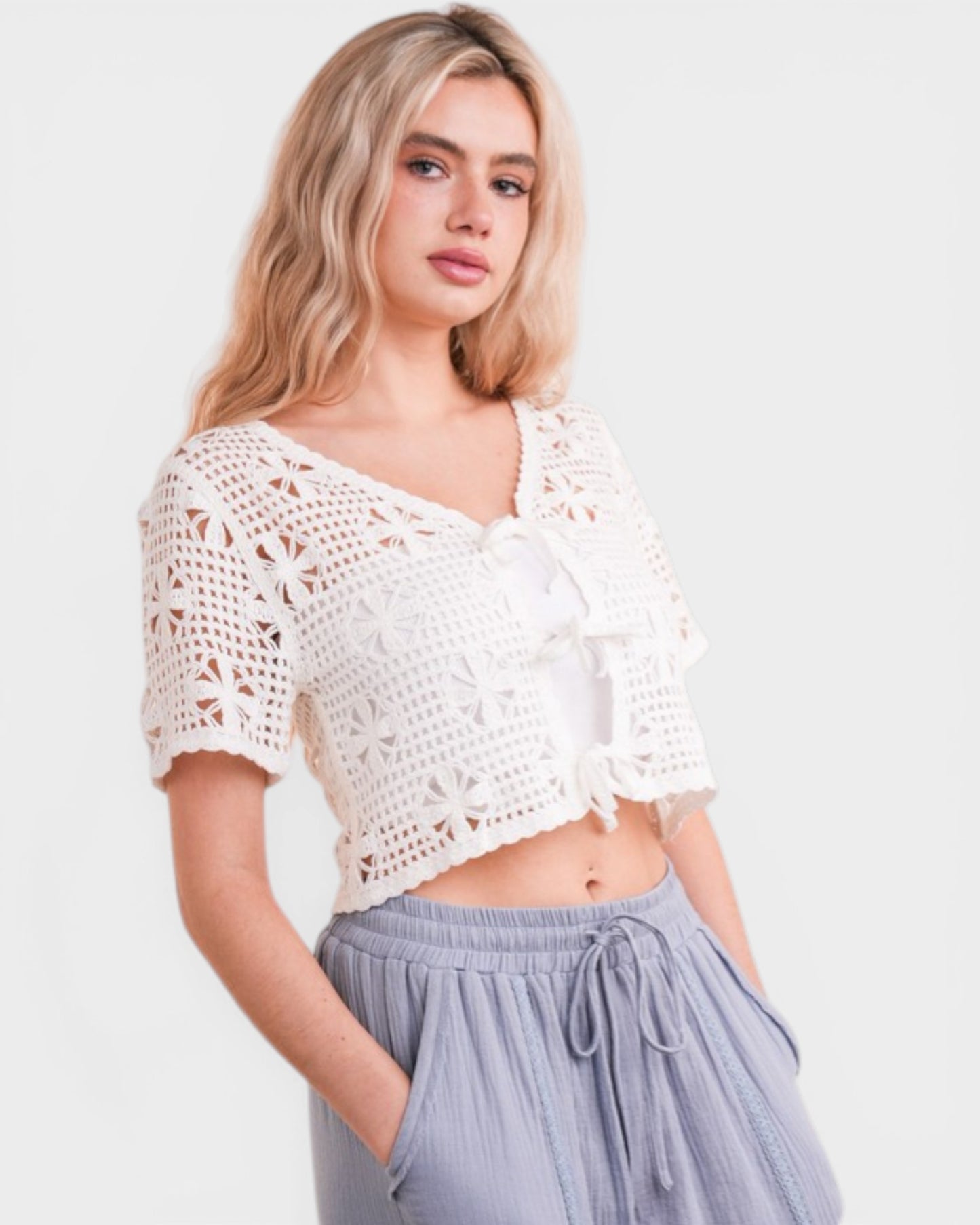 Woman wearing a white crochet top and light purple pants on a plain background