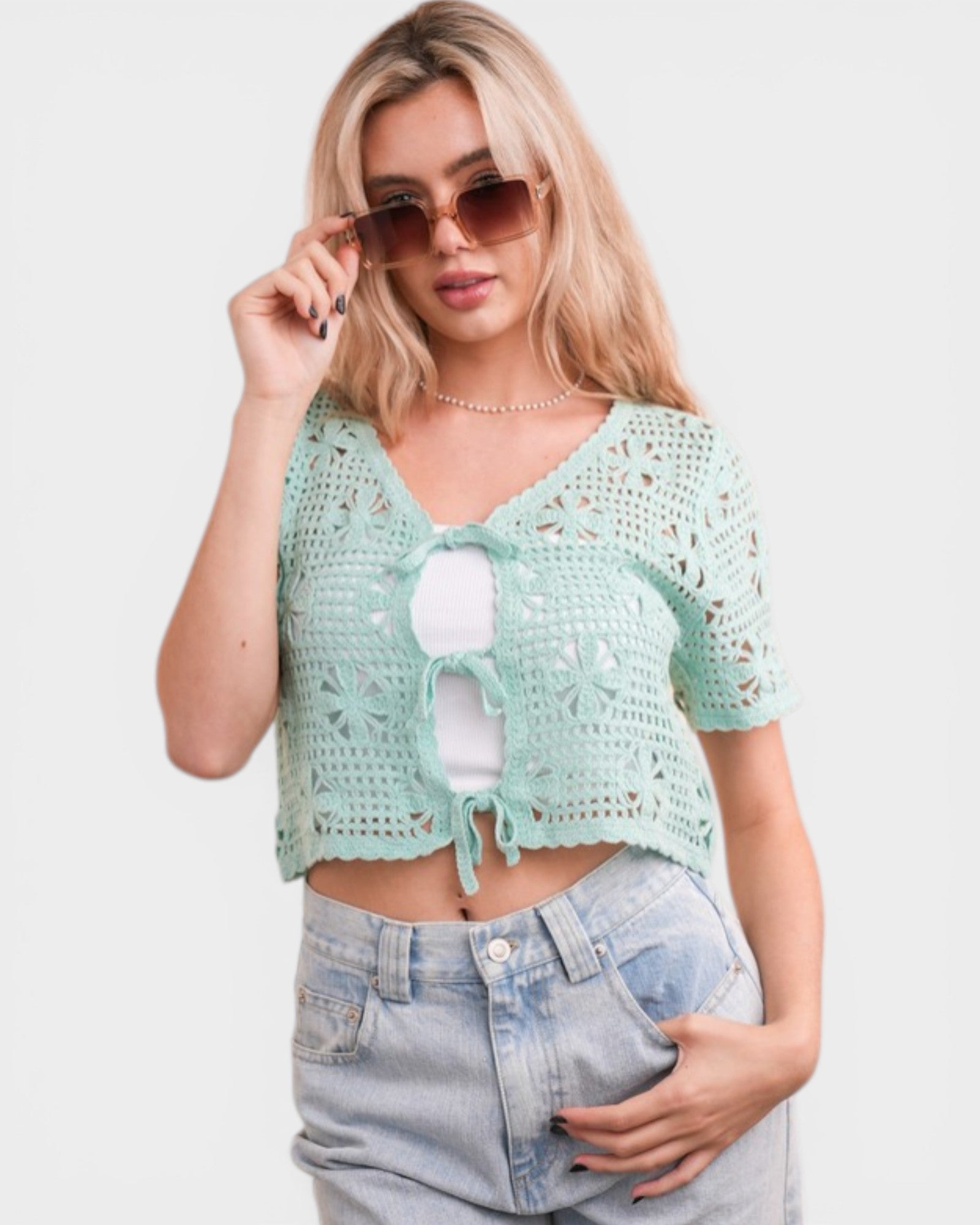 Woman wearing a light green crochet top and denim shorts on a white background