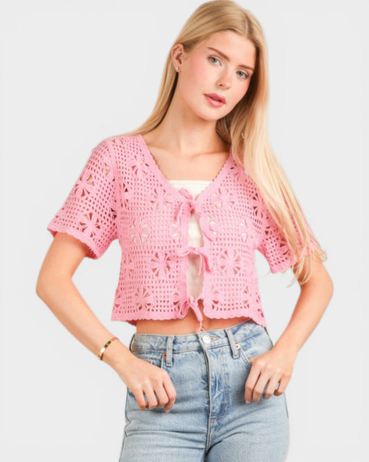 Woman wearing a pink crochet top and blue jeans on a light gray background