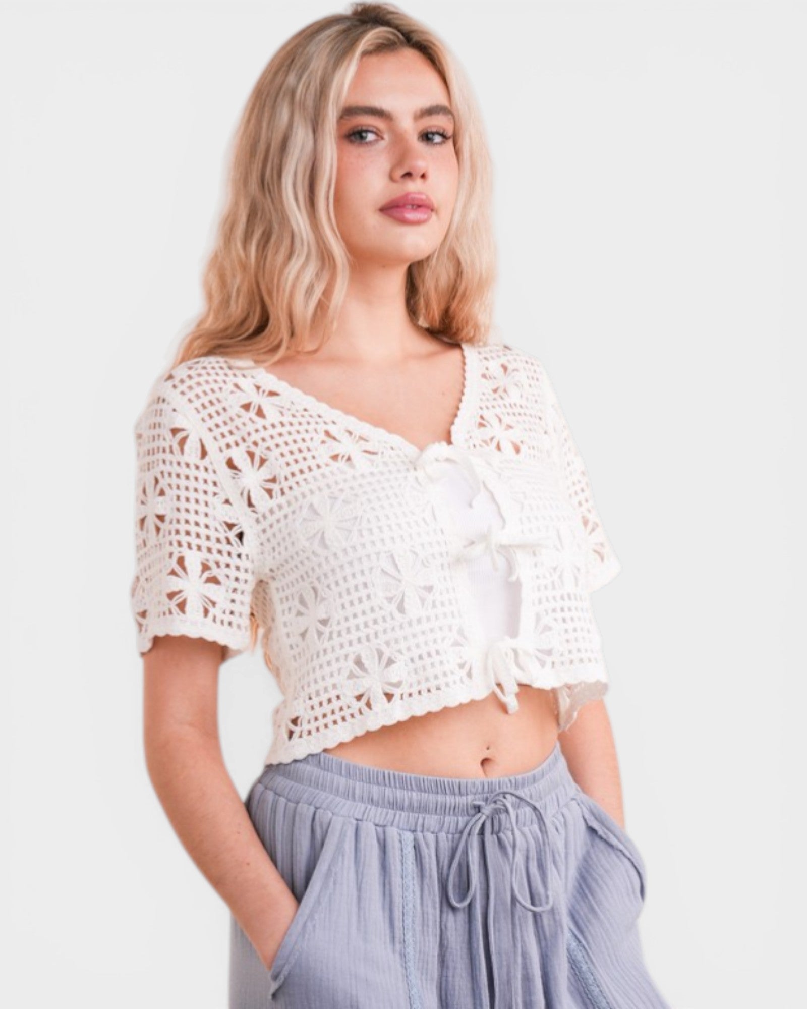 Woman wearing a white crochet top and light blue pants on a plain background