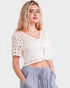 Woman wearing a white crochet top and light blue pants on a plain background