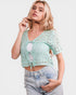 Woman wearing a light green crochet top and denim shorts on a white background