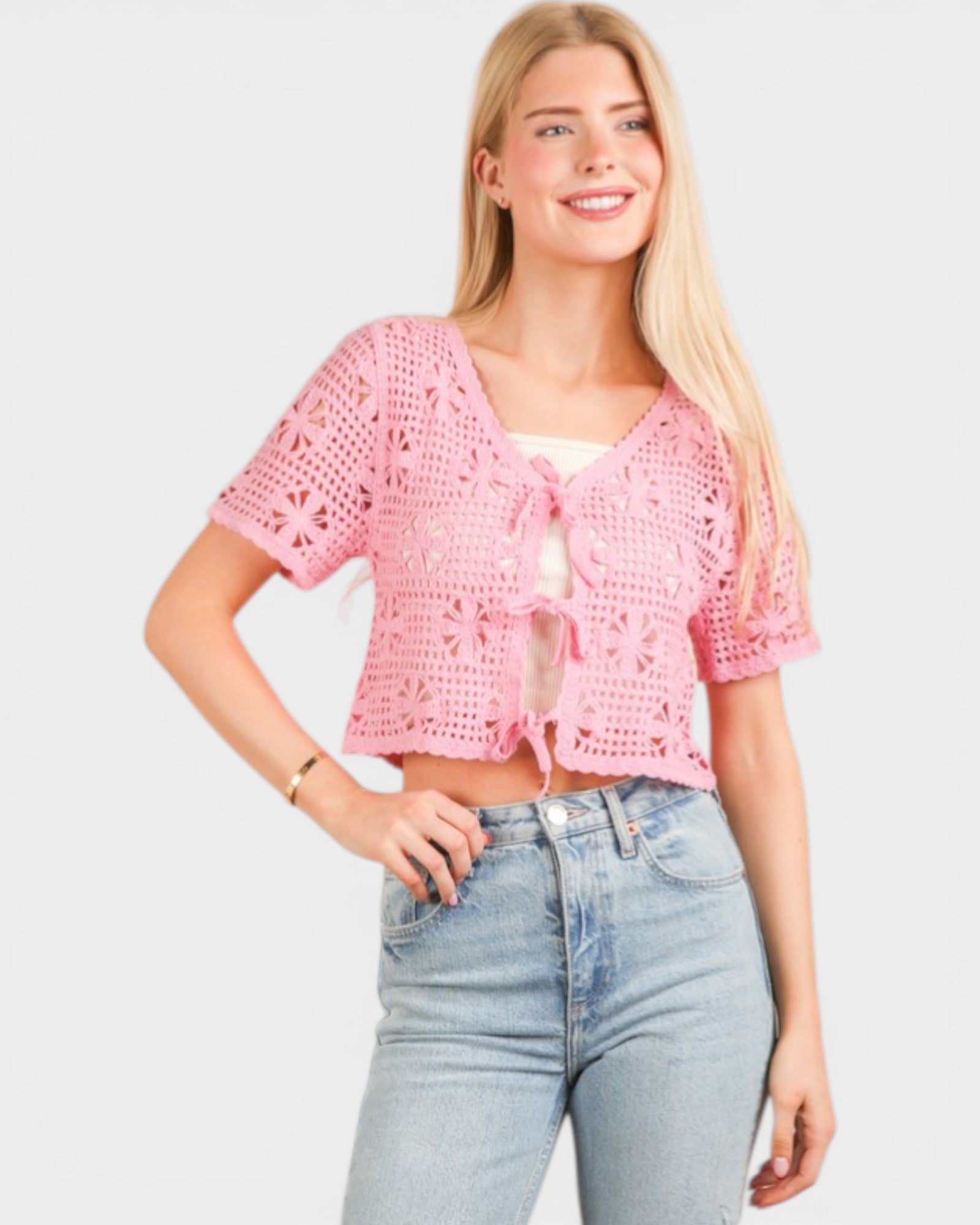 Woman wearing a pink crochet top and light blue jeans on a white background