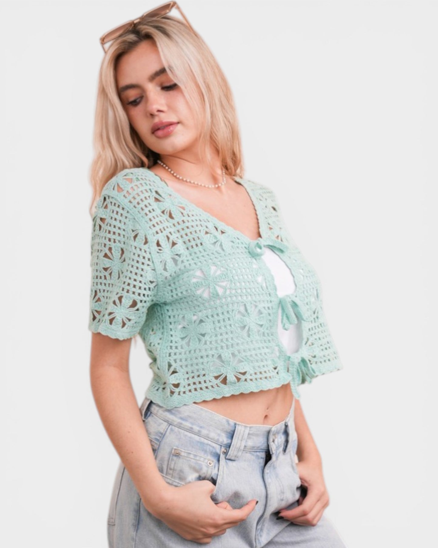 Woman wearing a light blue crochet top and jeans on a white background