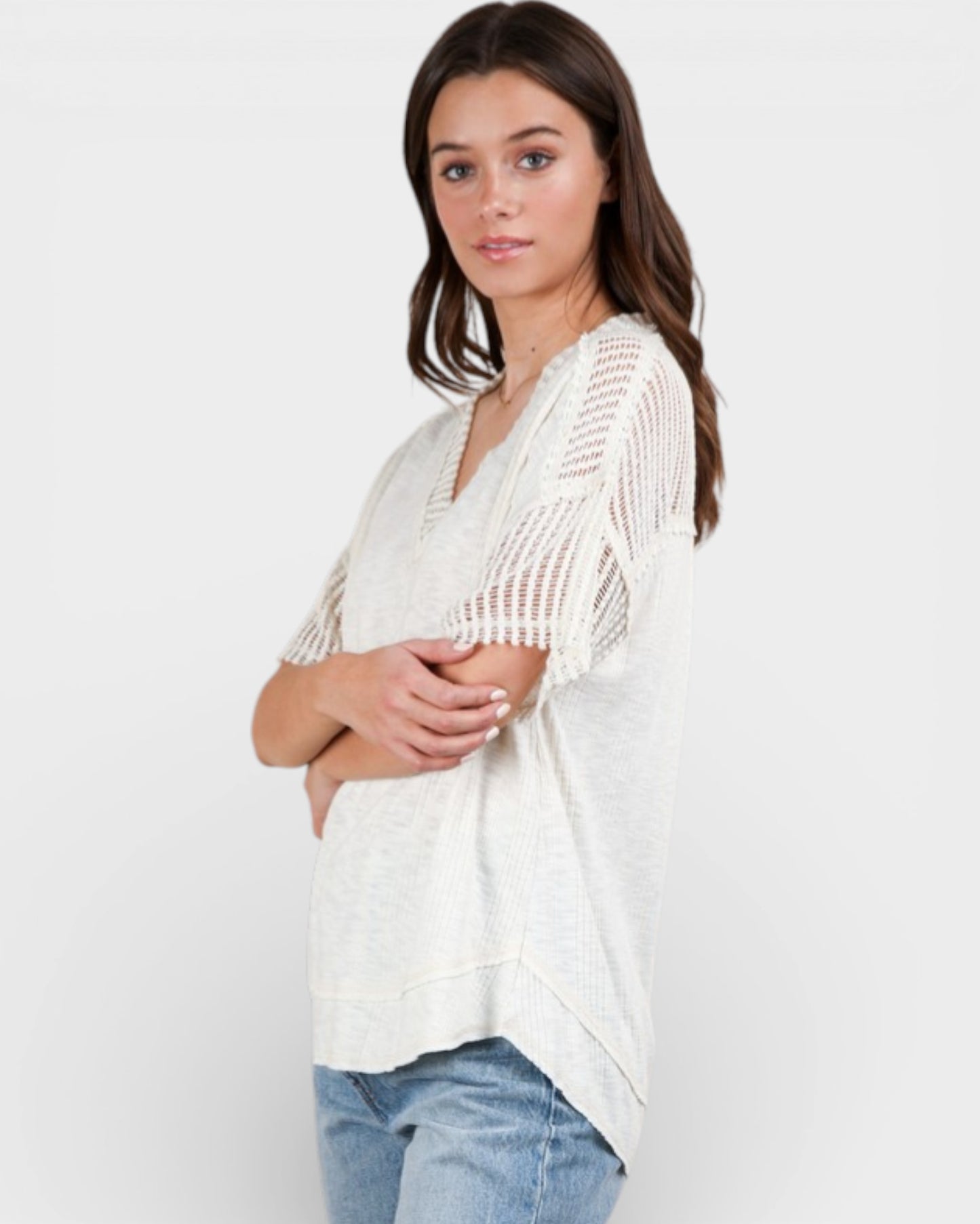 Woman wearing a white knit cardigan over a blue top on a plain background