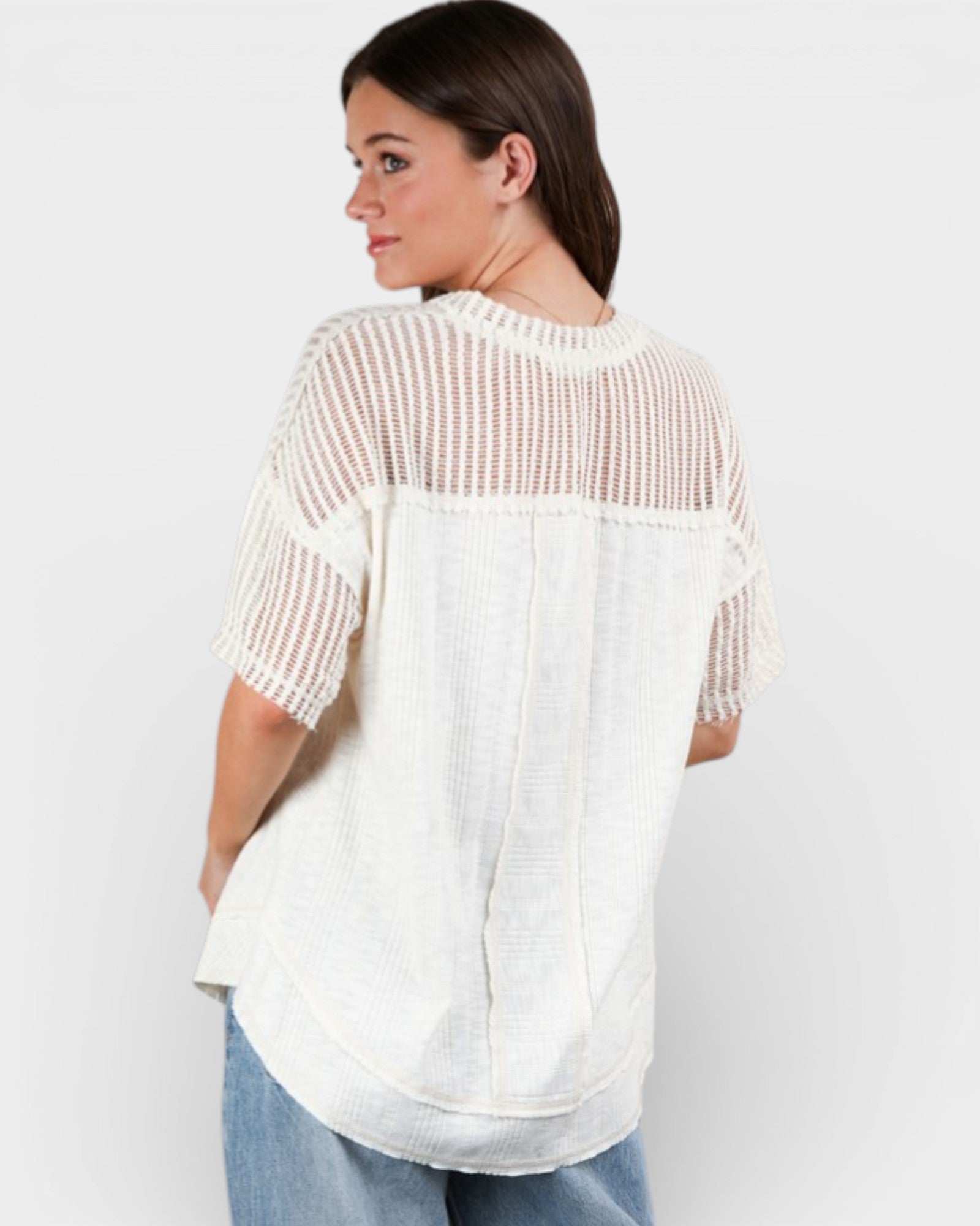 Woman wearing a white blouse with mesh sleeves on a plain background