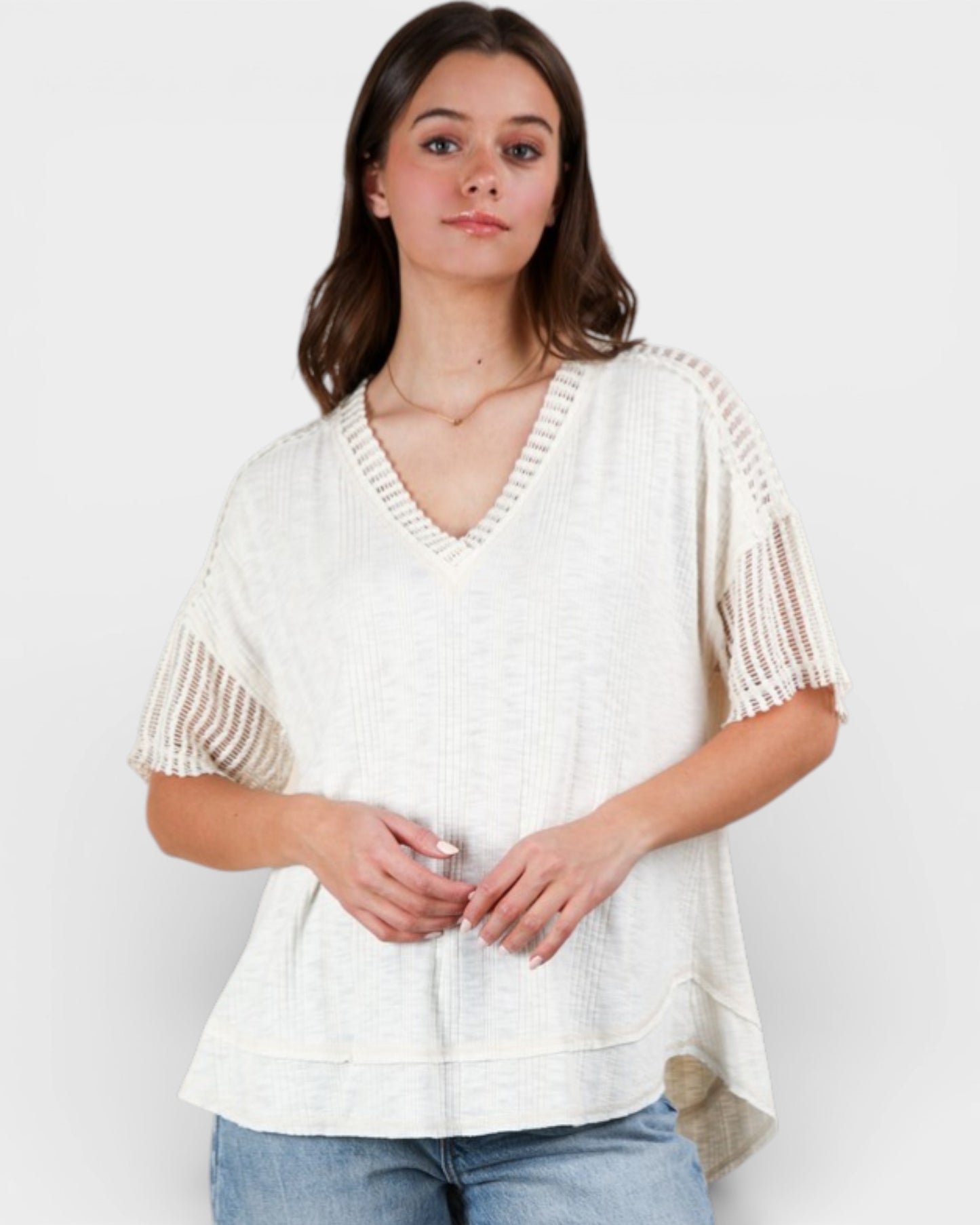 Woman wearing a white knit top with beige accents on a plain background