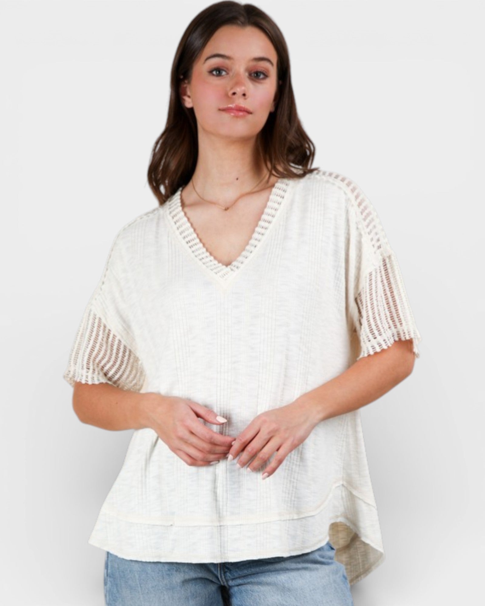 Woman wearing a white knit top with beige accents on a plain background