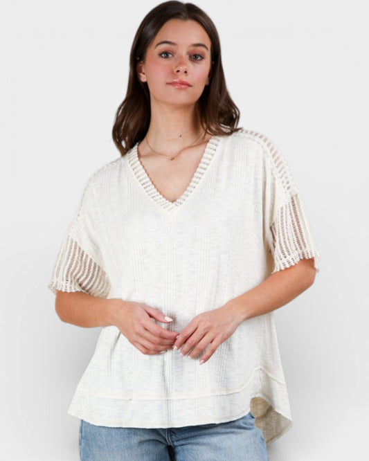 Woman wearing a white knit top with beige accents on a plain background