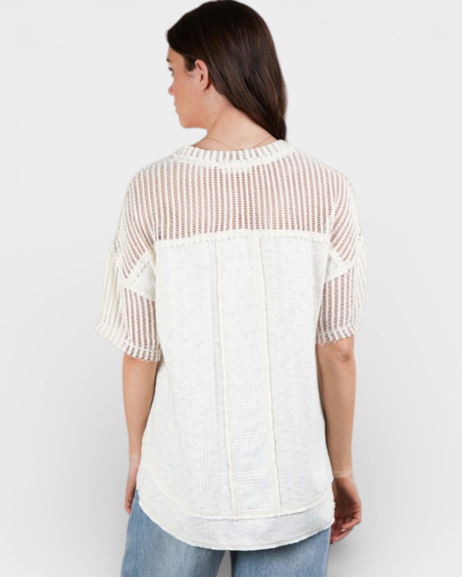 Woman wearing a white and beige patterned top on a plain background