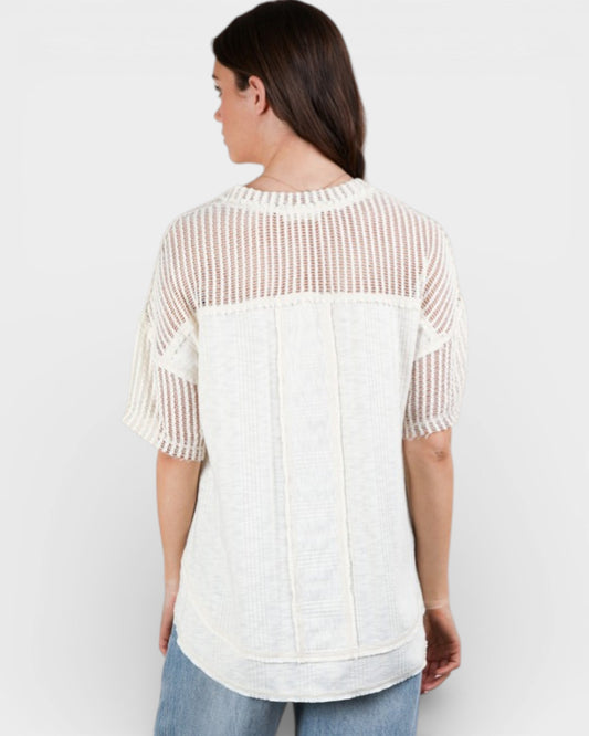 Woman wearing a white and beige patterned top on a plain background