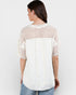 Woman wearing a white and beige patterned top on a plain background