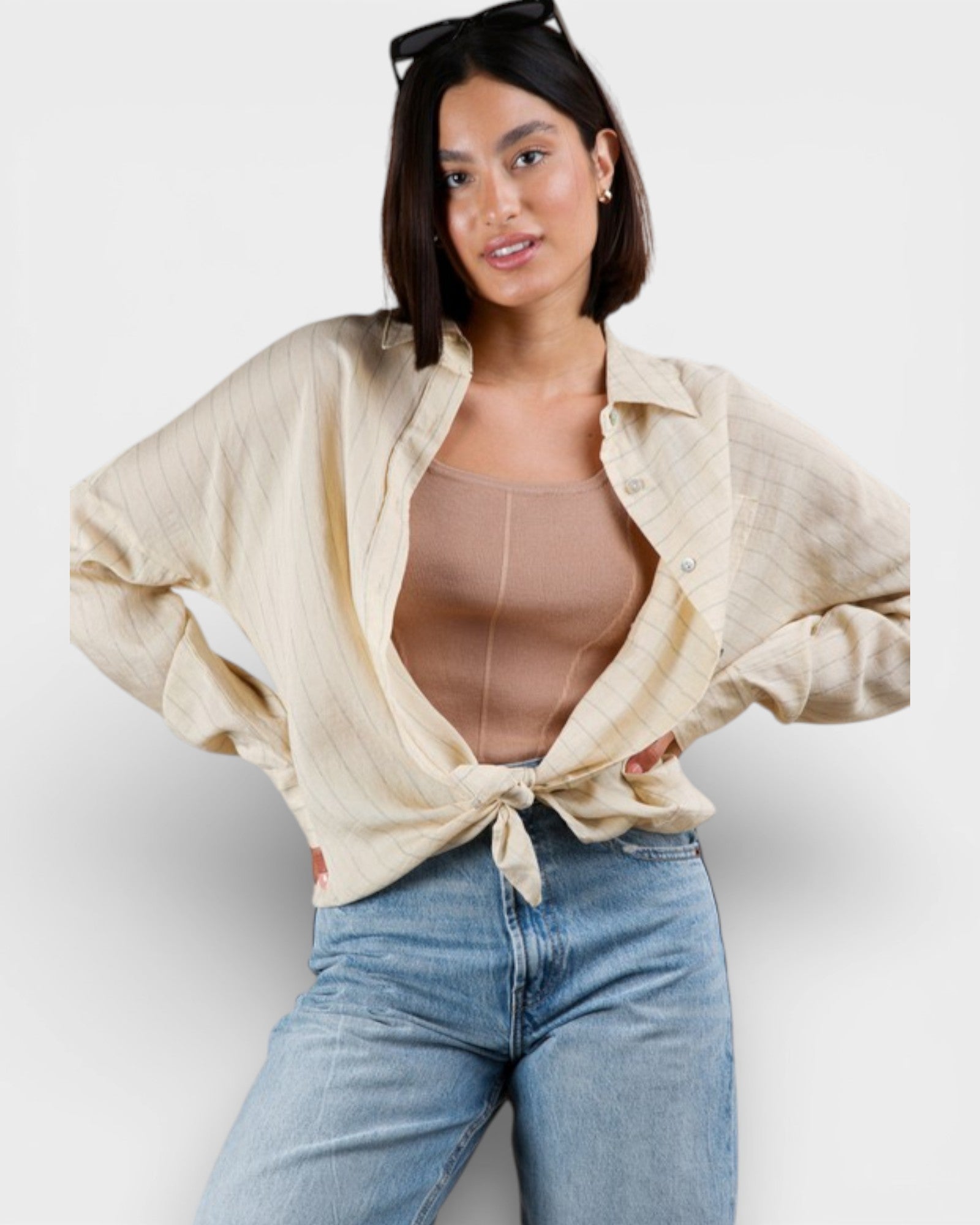 Woman wearing a beige shirt over a sheer top and blue jeans on a white background