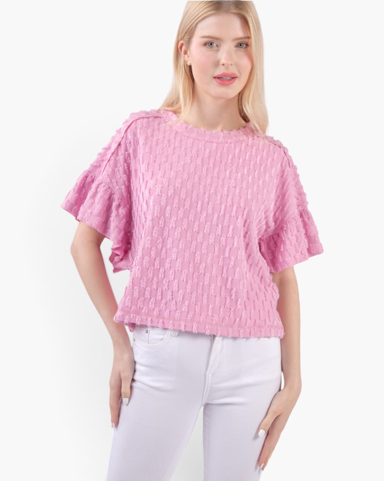 A woman modeling a pink textured short-sleeve top with ruffled sleeves and white pants against a plain white background.