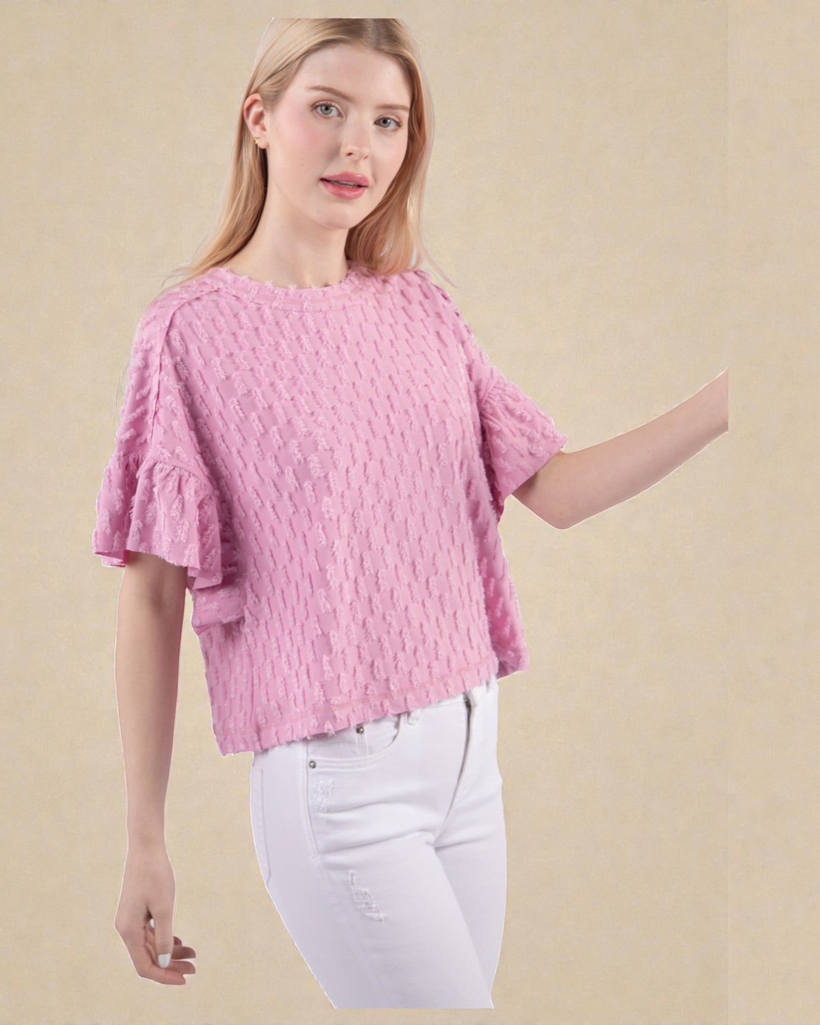 Woman wearing a pink textured top and white pants on a beige background