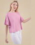 Woman wearing a pink textured top and white pants on a beige background