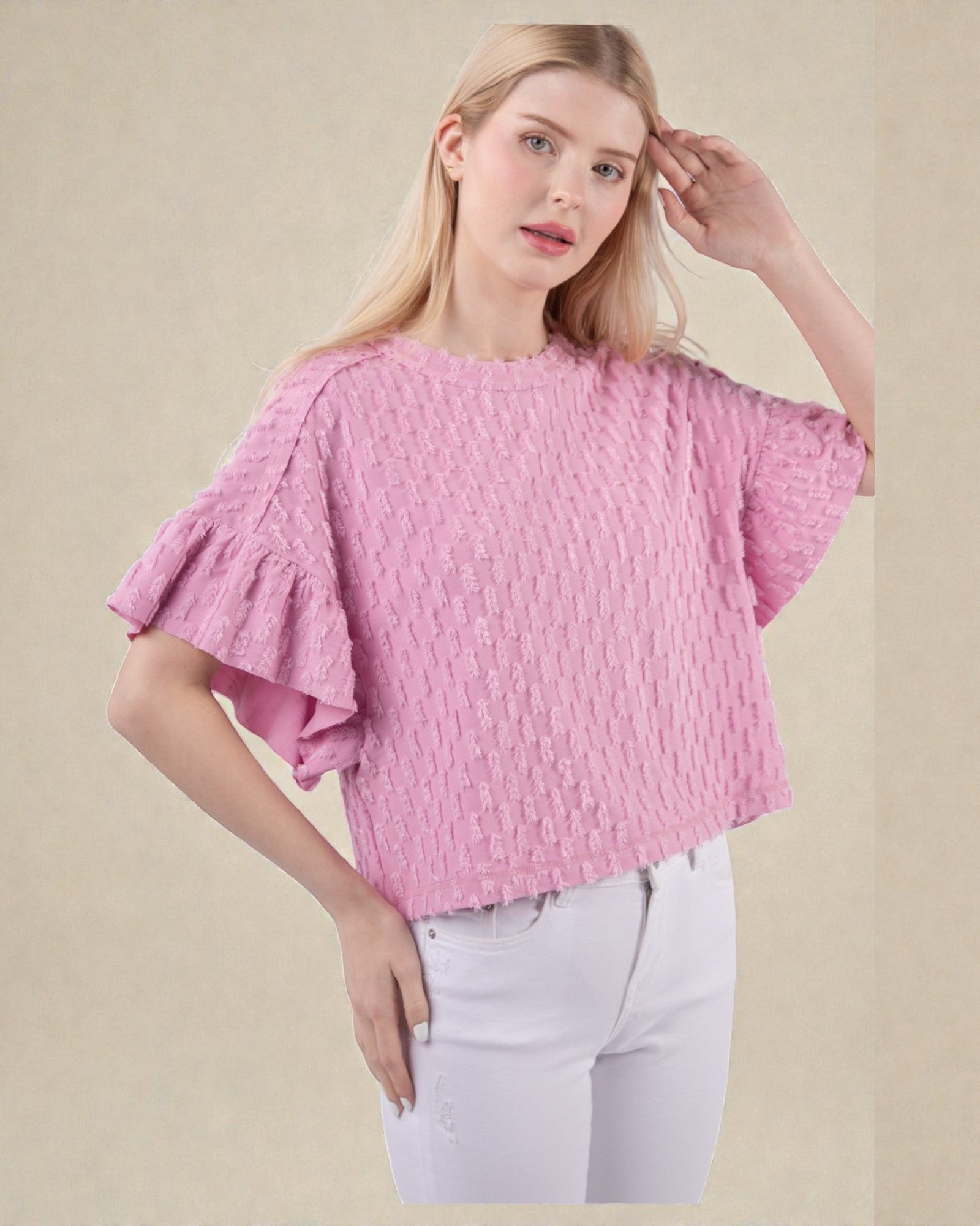 Woman wearing a pink textured blouse with ruffled sleeves on a beige background