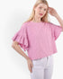 A woman wearing a pink textured short-sleeve top with ruffled flutter sleeves and white pants, photographed against a plain light background.