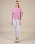 Woman wearing a pink textured top and white pants on a beige background