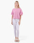 A woman modeling a pink textured short-sleeve top with ruffled sleeves, paired with white skinny jeans and white slide sandals, against a plain white background.